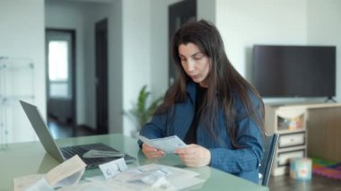 Ödenmemiş faturalar ve faturalarla çevrili, evde mali belgeleri okuyan endişeli bir kadın çalışırken stres ve mali sorunlar yaşıyor..