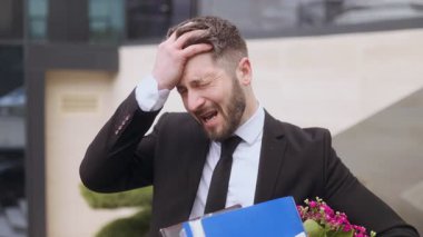 İşten çıkarıldıktan sonra duygusal olarak tükenmiş işçiler ellerinde kişisel ofis eşyalarıyla dışarıda duruyorlar ve stres, yenilgi ve derin üzüntü belirtileri gösteriyorlar..