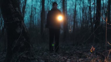 Gece bir ormanın ürkütücü sessizliğinde, bir adam elinde fenerle durur, ışık karanlığın içinden geçer ipuçlarını ya da görünmeyen bir şeyi arar..