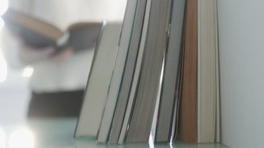 Bir el kitap yığını üzerine bir kitap koyar, kitaplarla çevrili, bilgiye olan tutkuyu, entelektüel merakı ve bilimsel atmosferi sembolize eder..