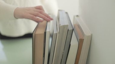 Bir insan eli, daha sonra ne okuyacağını seçmenin basit ve entelektüel eylemini vurgulayan bir kitap yığınından bir kitap seçer..