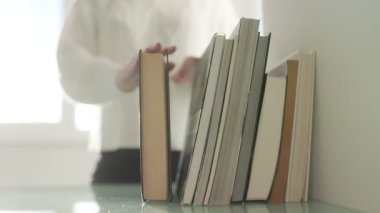 Bir el, bir yığın kitapla etkileşime girer, bilgiyi, merakı ve edebiyatın günlük hayattaki ebedi cazibesini sembolize eder..