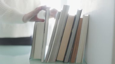 Karar verme sürecinin yakın plan çekimi. Bir el, temiz beyaz bir masa üzerindeki zarif bir kitaptan dikkatlice bir kitap seçerken..