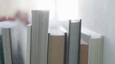 Bir bireyin eli istiflenmiş kitap seçimiyle etkileşime girer, merak, eğitim ve edebiyatın daimi cazibesi temalarını uyandırır..