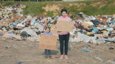 Çevre koruma ve değişimi savunan, kirliliği durdurun ve gezegeni kurtarın yazan tabelalar taşıyan bir anne ve kız..