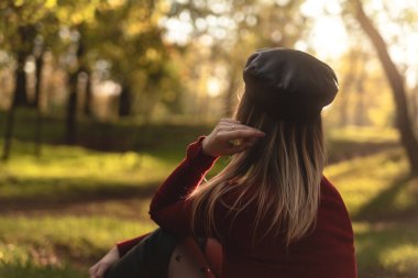 Kırmızı golfteki genç ve güzel kadın sonbaharda parkta güneşin tadını çıkarıyor.