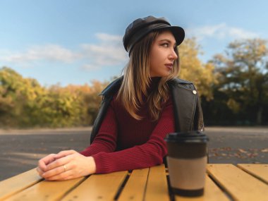 Kırmızılı genç ve güzel bayan sonbaharda parkta bir bardak sıcak çay içiyor.