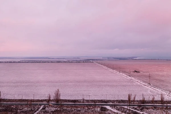 Clear snowy field with pink sunset and the sea in the distance