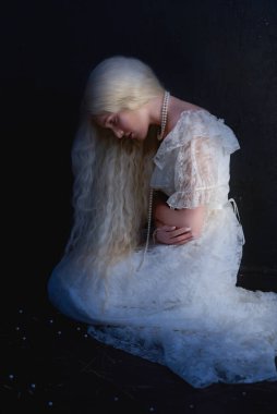 Beyaz saçlı, 19. yüzyıldan kalma beyaz elbiseli, boynunda kolyesi olan genç bir kız. Stüdyo çekimi