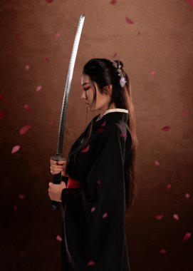 Japon kadın samuraylar kimono giyiyorlar ve kahverengi arka planda katana tutuyorlar ve çiçek yaprakları. Japon kültürü