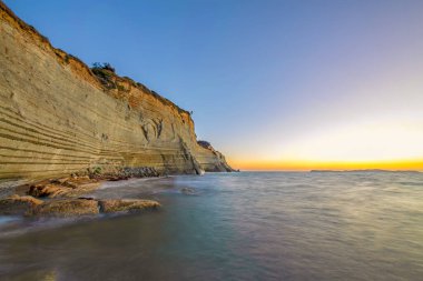 Uzun pozlama kayalar, deniz, gün batımı ve deniz günbatımı sırasında sahilde dalgalar. Güzel alacakaranlık kontrast arka plan. Ünlü Logas beach cliff Corfu Island, Yunanistan