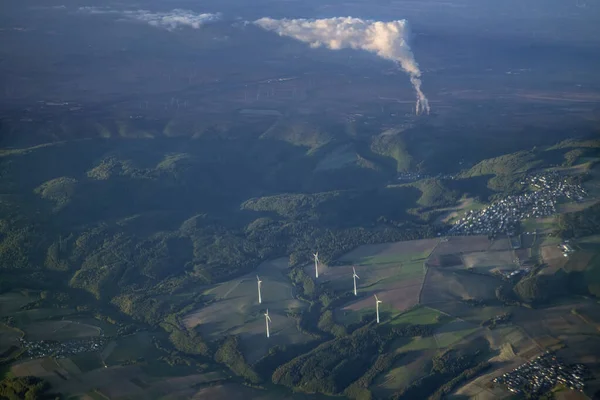 Aerial view of wind turbines on a field with white smoke from the pipes of a thermal power plant on background. Concept of alternative sources of electricity