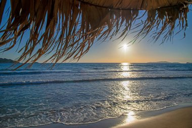 Gün batımında şemsiyeden samanların yakın görüntüsü ve bulanık arkaplanda mavi deniz. Seyahat, tatil ve turizm kavramı