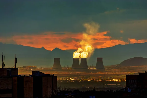 Mysterious silhouette of the Armenian Nuclear Power Plant at dramatic sunset and the smoke illuminated with sunlight, view from Yerevan, Armenia. Beautiful sunset. Perfect background for a text