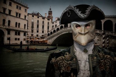 İtalya, Venedik 'te dramatik günbatımında, Grand Channel' da Rialto Köprüsü ve Gondola 'ya karşı eski moda maske takan tanınmamış ciddi bir adamın portresi bulanık bir arka plan.
