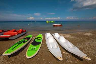 Korfu, Yunanistan - 01 Eylül 2022: Kum plajındaki turistler için renkli kanolar, bisiklet katamaranları açık sarı ve yeşil renkli arka planda mavi gökyüzü altında şişirilebilir cazibe