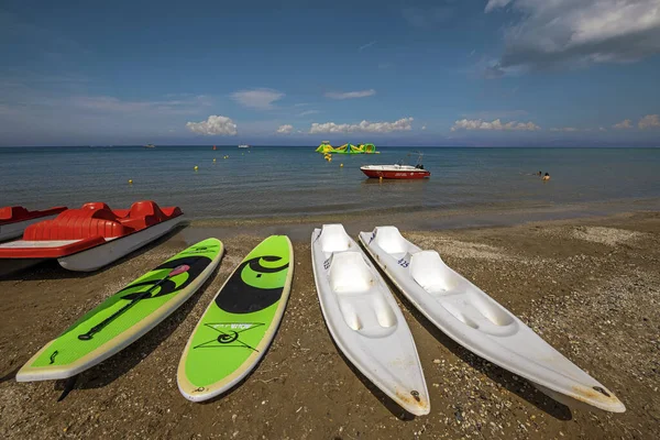 希腊科孚 2022年9月1日 一排排五彩斑斓的独木舟和自行车船在蓝色天空下蔚蓝的大海背景下 为海滩上的游客提供明亮的黄色和绿色充气吸引物 — 图库照片