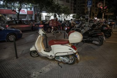 Selanik, Yunanistan - 13 Eylül 2022: Vintage beyaz Vespa gece kasabasında sokağa park edilmiştir. Ünlü İtalyan scooter 'ı. Bulanık bir arkaplanda şehir trafiği