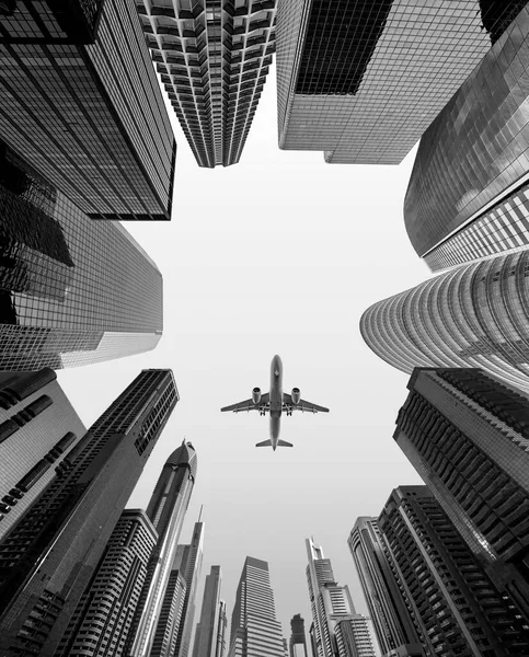 Airplane flying over business skyscrapers of financial center. Travel, economy, cargo, transportation concept. Low wide angle perspective view, black and white photography