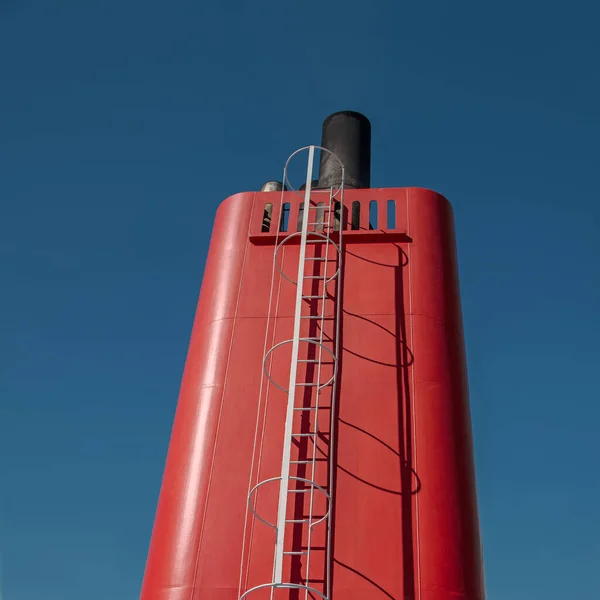 Contrast minimalist scene with big red ship funnel illuminated with bright sunlight against deep blue sky background