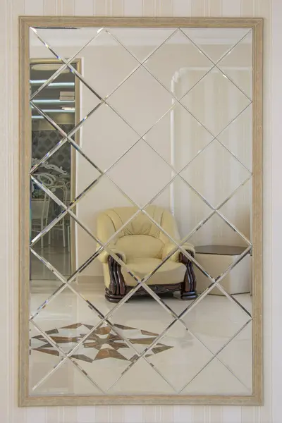 Glamour interior with beige leather armchair and coffee table on marble mosaic floor reflected in stylish big mirror created from multiple square faceted fragments. Abstract beautiful background
