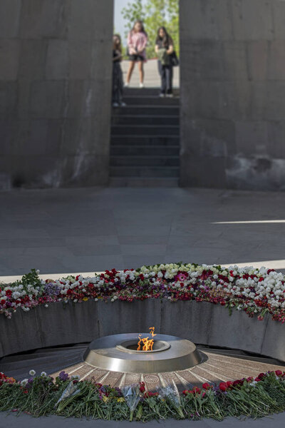 Unrecognizable girls on blurred background mourn at the Eternal Flame at the Armenian Genocide Memorial Monument surrounded with colorful flowers in Tsitsernakaberd, Yerevan, Armenia