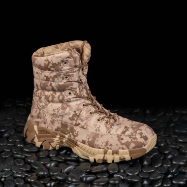 Siyah çakıl taşları üzerinde koyu arka planda izole edilmiş yüksek taktiksel dayanıklı çöl botu. Kaygan değil, dantelli açık ayakkabılar yürüyüş, yürüyüş, av kıyafetleri için.