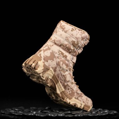 Siyah çakıl taşları üzerinde koyu arka planda izole edilmiş yüksek taktiksel dayanıklı çöl botu. Kaygan değil, dantelli açık ayakkabılar yürüyüş, yürüyüş, av kıyafetleri için.