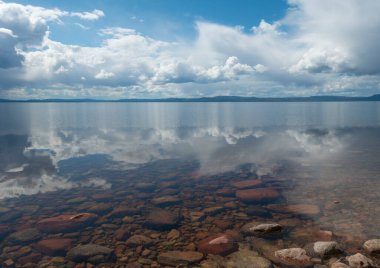 Clouds in blue sky reflected in clear water of lake
