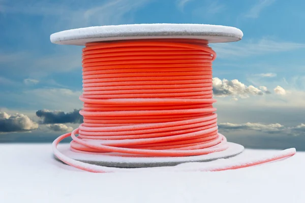 木制电缆鼓 雪中有橙色电缆 蓝天上有蓬松的云彩 图库图片