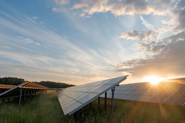 stock image Solar panels at orange sunset, with blue sky and fluffy clouds