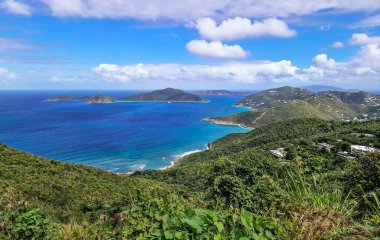 Bereketli yeşil tepeleri, berrak mavi denizi, parlak gökyüzünü ve ufukta adaları olan tropik bir manzara.
