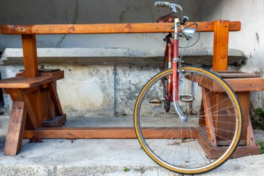 Ahşap bir masanın yanına park edilmiş kırmızı antika bir bisiklet ve kırsal alanda banklar..