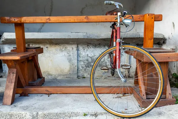 Ahşap bir masanın yanına park edilmiş kırmızı antika bir bisiklet ve kırsal alanda banklar..
