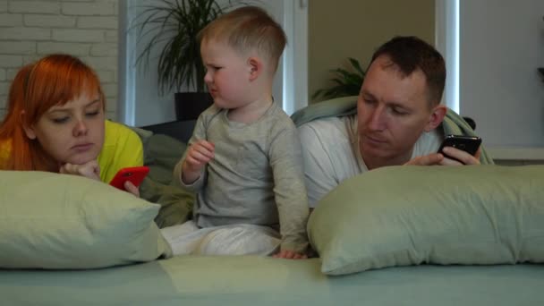 Young Parents Little Boy Bed Mom Dad Look Screens Phones — Vídeo de Stock