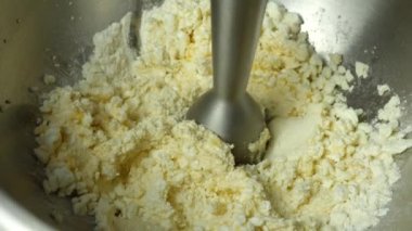 The cook interrupts the mass with homemade cottage cheese, chicken egg, sugar and flour with a blender. The process of making curd pancakes close-up. Slow motion.
