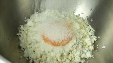 The cook pours flour through a sieve into a bowl in which sugar, a raw chicken egg, homemade cottage cheese. The process of making curd pancakes close-up.