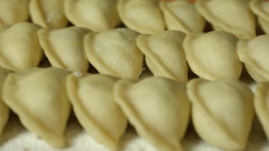 Ukrainian national dish. Raw handmade dumplings on a wooden kitchen board sprinkled with flour. Vareniki are stacked in neat rows. Close-up. Movement to the right.