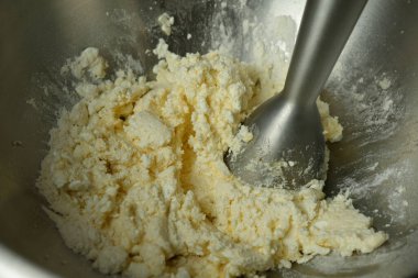 The cook beats a mass of homemade cottage cheese and eggs with a mixer in a large metal bowl. Close-up.