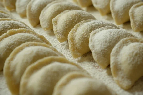 Raw handmade dumplings on the surface with flour, sprinkled with flour on top. Beautiful rows of dumplings. Ukrainian national dish. Close-up.