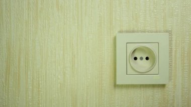 A man's hand inserts a black electric plug into a white plastic socket on the wall. Place for text.