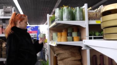 Shelves in a store with interior and home decor items. In the background, out of focus, a girl chooses a glass flowerpot.