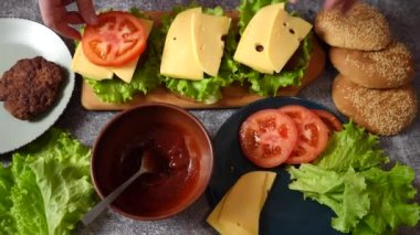 The hands of the cook collect three burgers on a wooden board. The process of making burgers. Shooting from above.