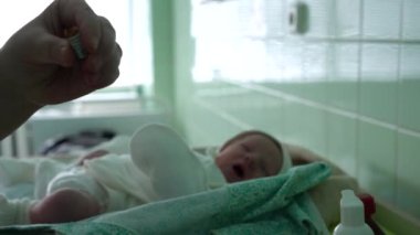 Eldivensiz bir doktor yeni doğmuş bir çocuğa aşı yapmak için şırıngaya aşı koyar. Arka planda yeni doğmuş bir bebek çığlık atıyor. Aşıyı hastanede yaptık. Sağlık standartlarının ihlali