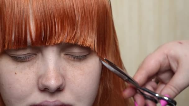 美容室ではさみで赤い髪のヨーロッパの女の子の前髪をカットします フロントビュー クローズアップポートレート — ストック動画
