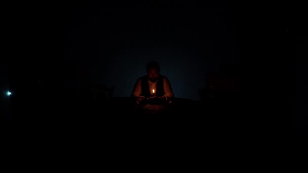 夕暮れの男がテーブルに座り ろうそくを手に持って炎を見ている ちらつきの光 高品質のフルHd映像 — ストック動画
