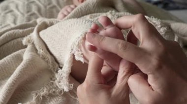 Anne, yeni doğmuş bebeğinin küçük ayağının parmaklarını sayıyor. Bir bebeğin ayağına yakın çekim. Kadının eli çocuğun bacağını gıdıklıyor.