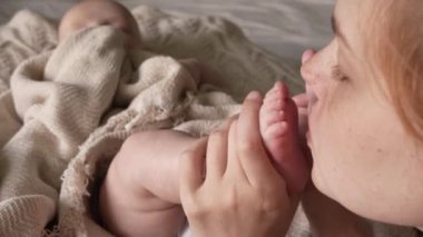 Anne bebeğinin küçük ayaklarını öpüyor. Yakın plan. Küçük çocuğun yüzü bulanık.