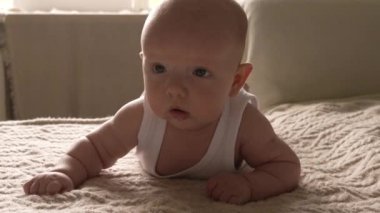 Yeni doğmuş küçük bir çocuk örgü örmüş bir battaniyenin üzerine uzanmış, gülümsüyor ve salya akıtıyor. Yakın plan..