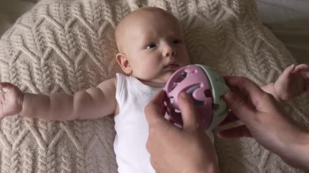 Маленький Новорожденный Мальчик Лежит Вязаной Подушке Кокона Смотрит Игрушечный Мяч — стоковое видео